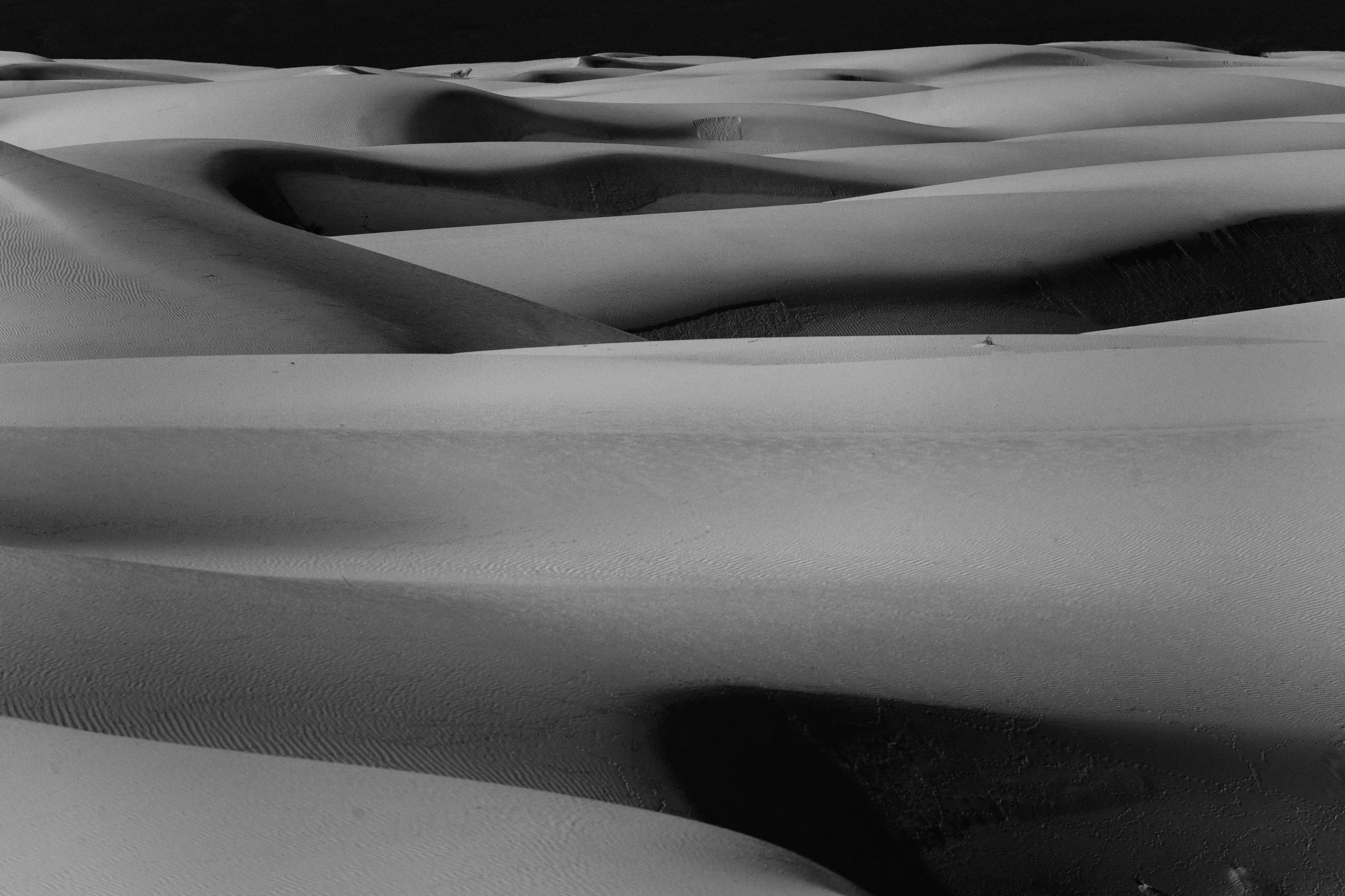 Black-and-white view of rolling gypsum dunes under a dark sky.