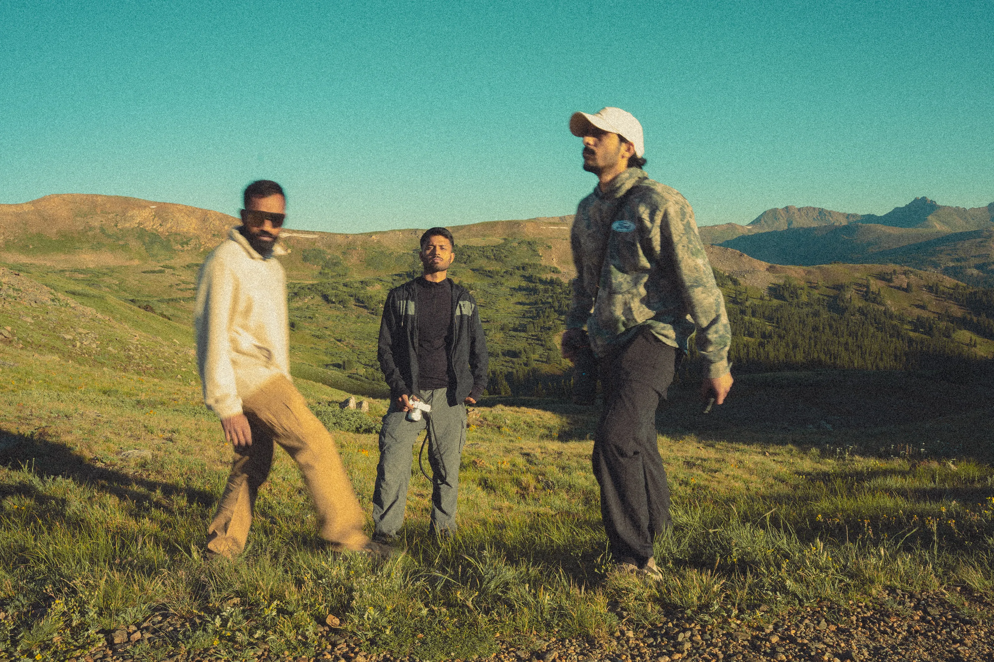 Three friends stand in an alpine meadow under a deep blue sky.
