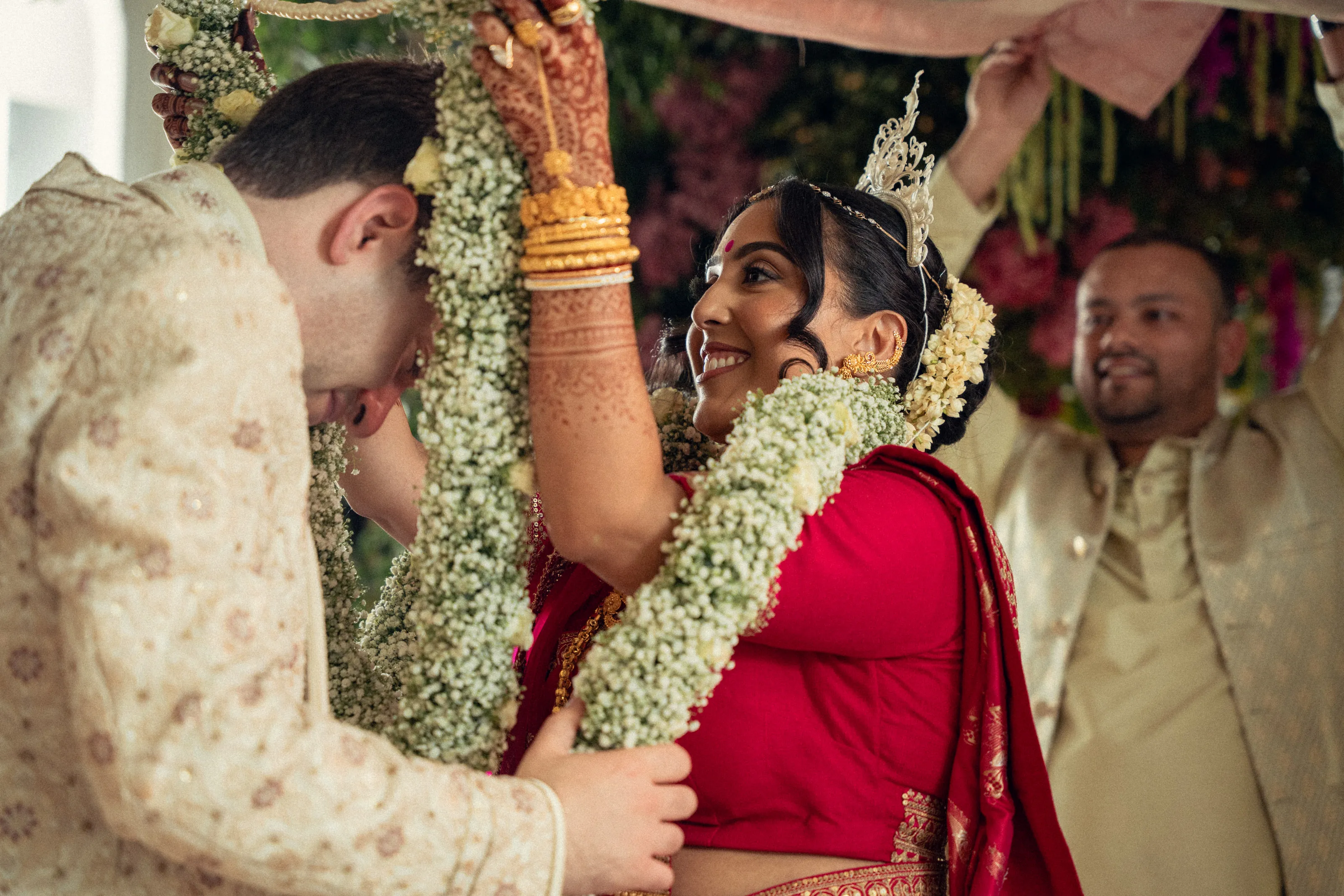 The bride and groom exchange flower garlands, smiling, during the ceremony.
