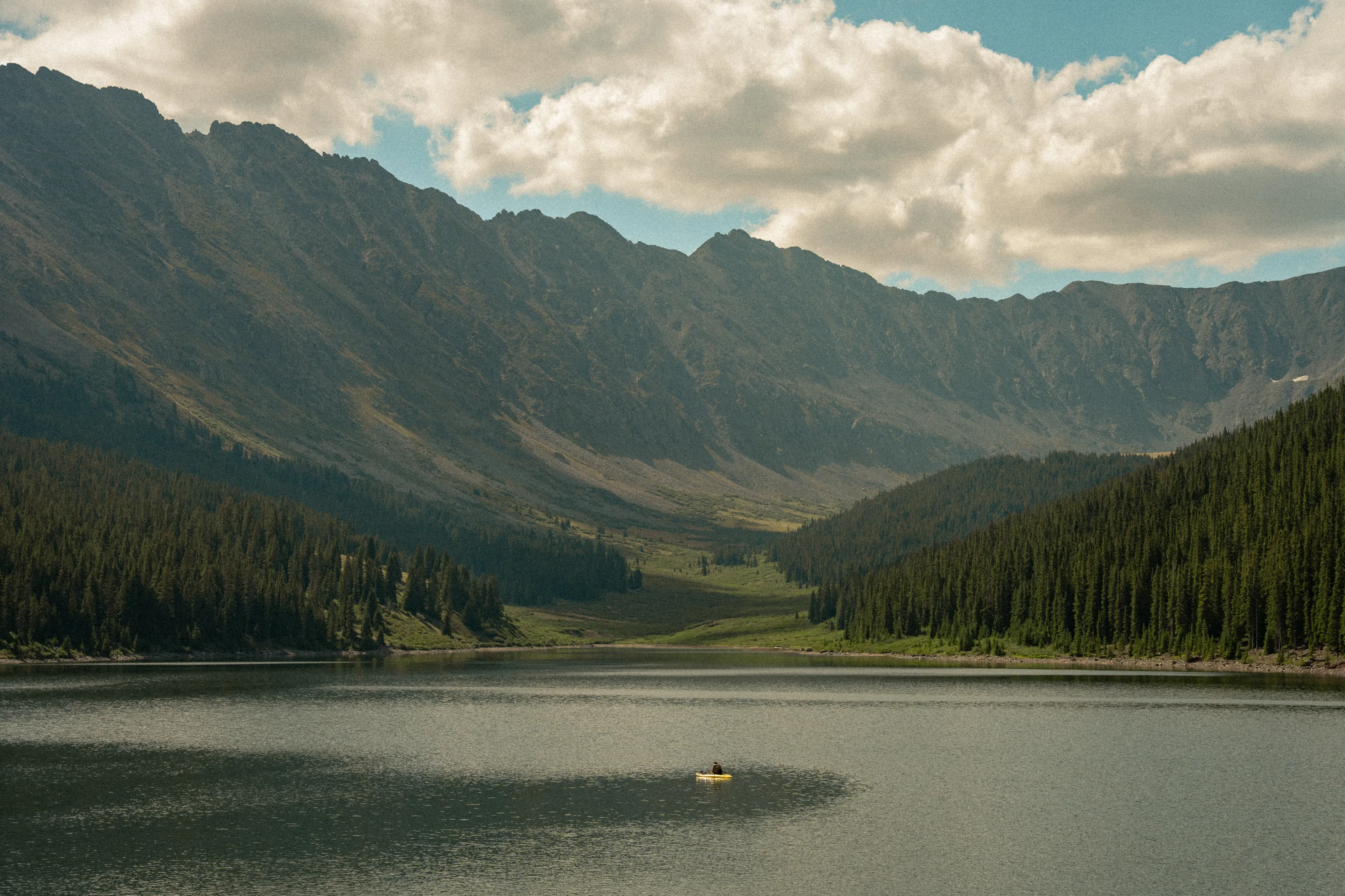 A still mountain lake beneath a long ridge of peaks, a small boat on the water.