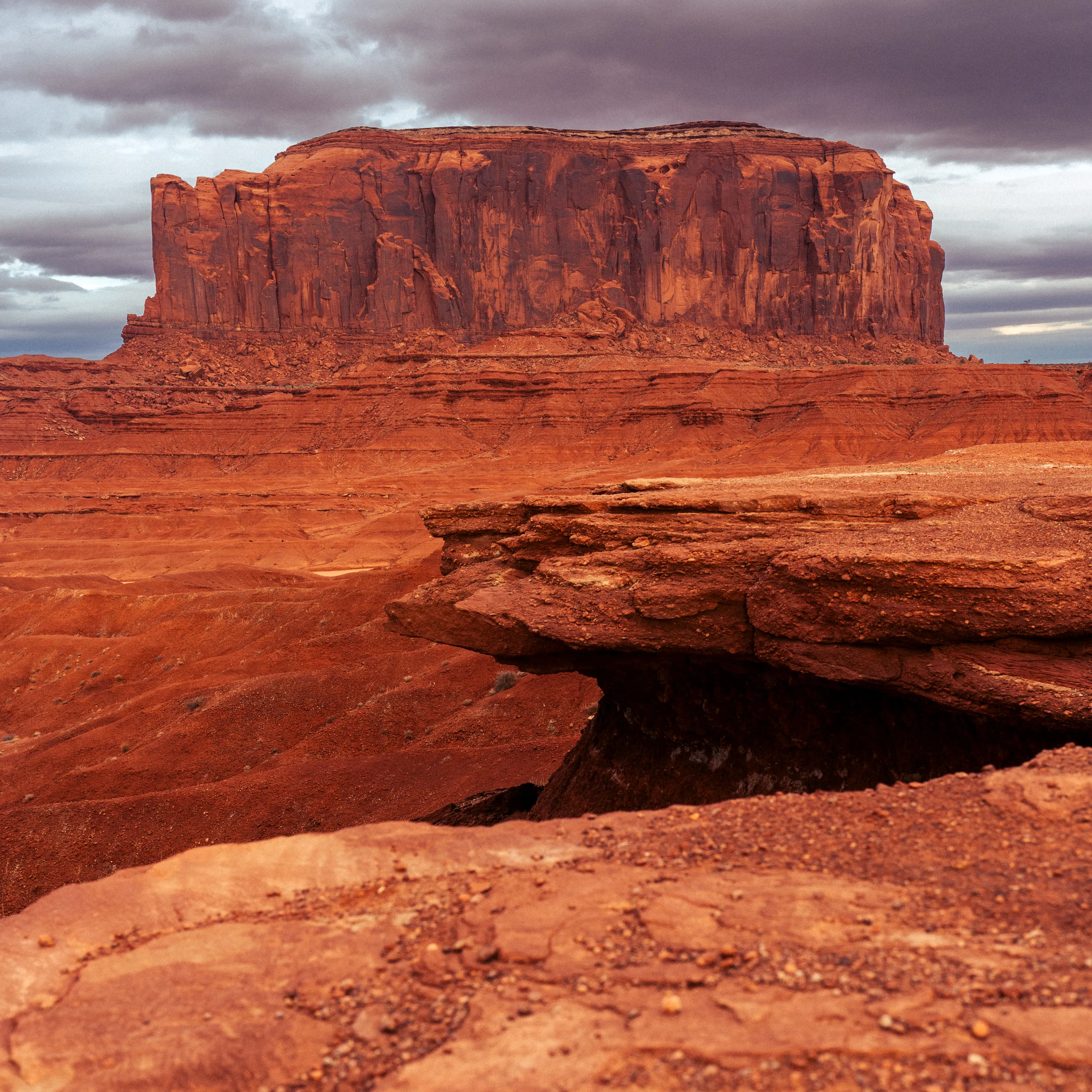 A flat-topped red mesa above a sandstone ledge under a stormy sky.