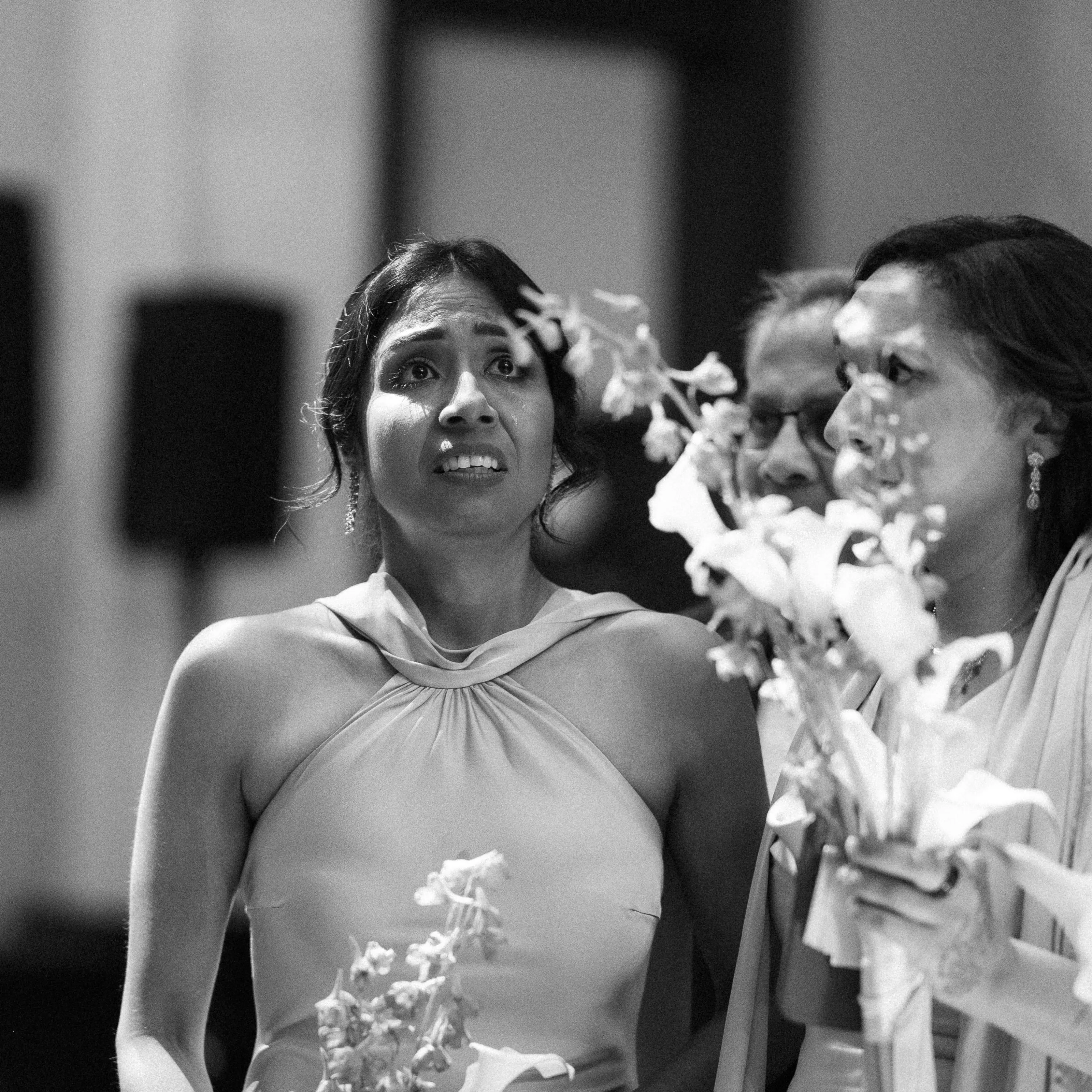 Black-and-white photograph of a guest with tears in her eyes, holding white flowers.