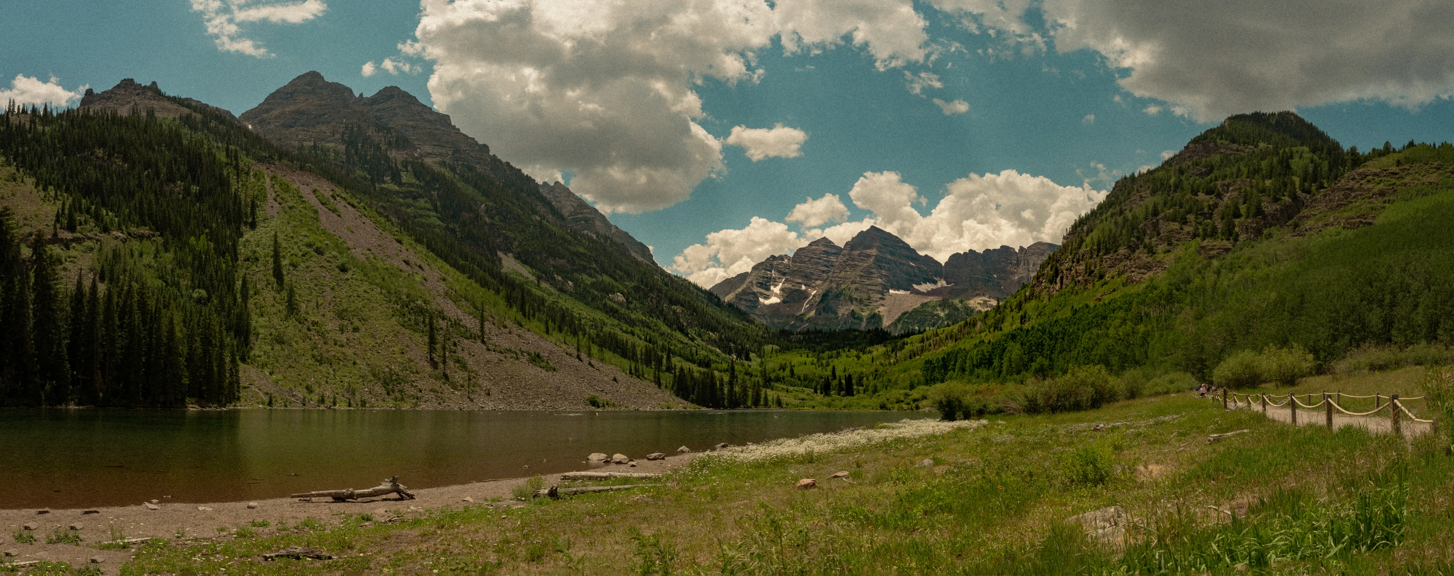 A wide panorama of a green valley leading to snow-streaked peaks.