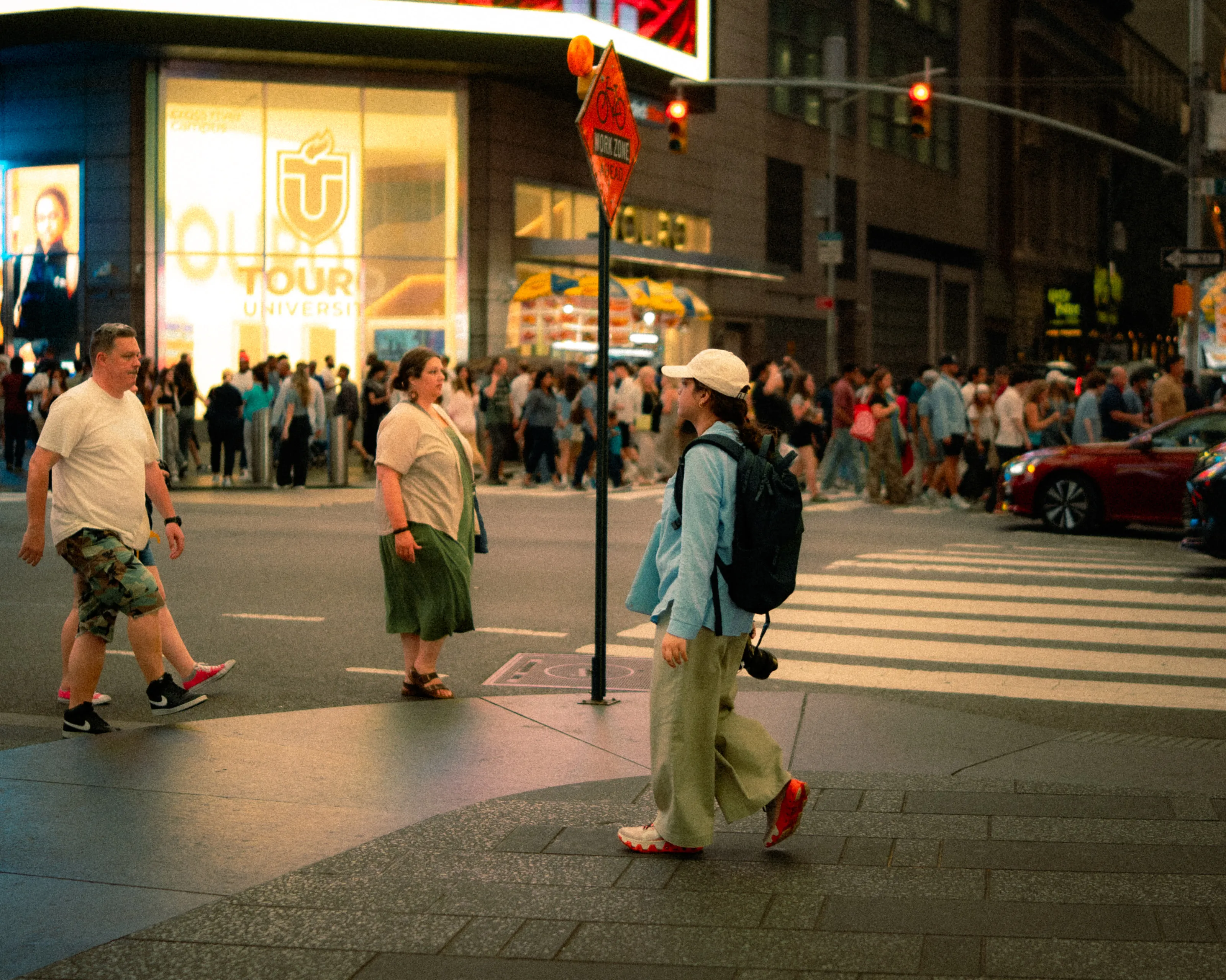 A crowd spills across a street at dusk beneath bright shop signs.