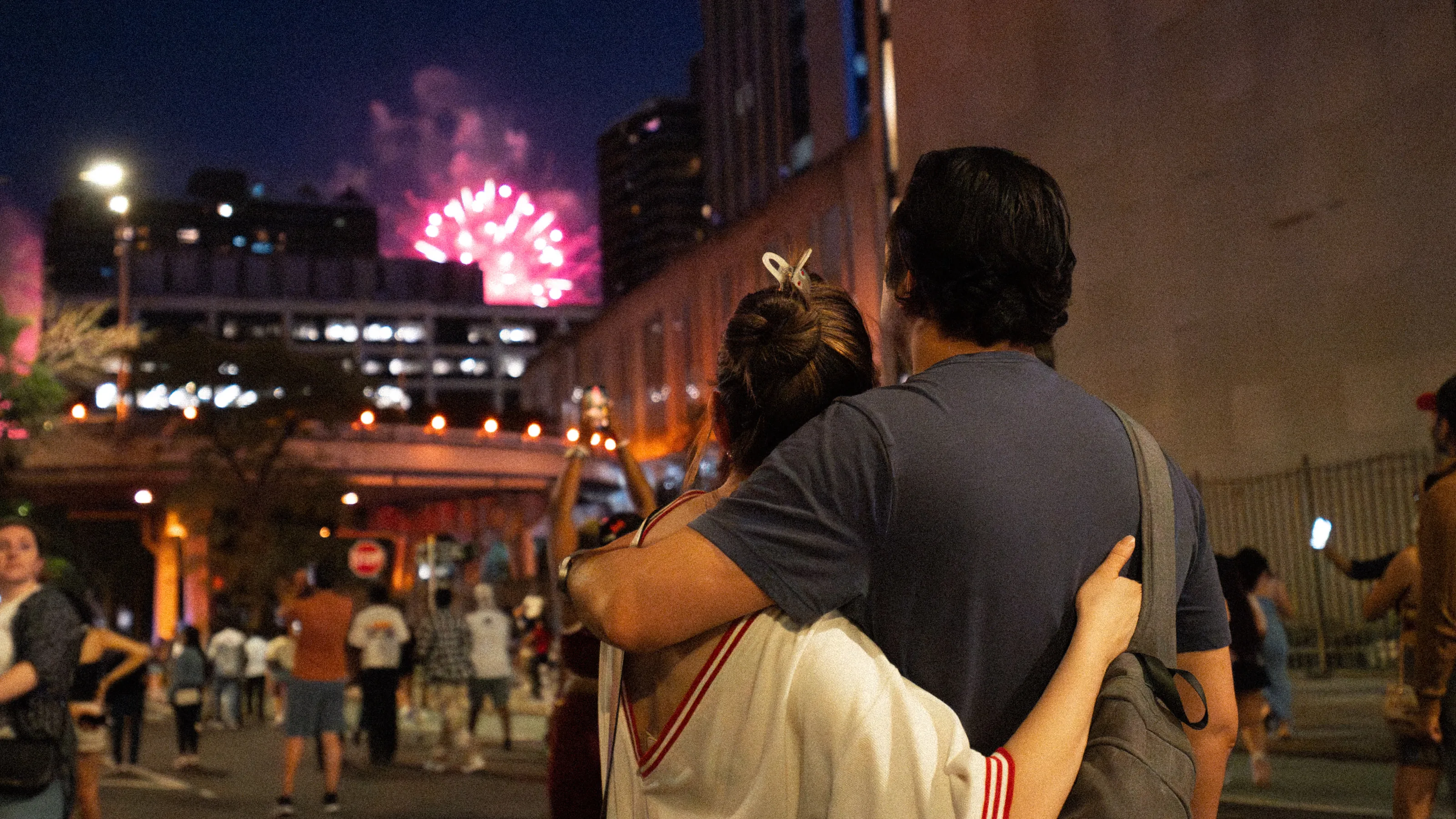 A couple embraces as fireworks light the sky beyond the crowd.