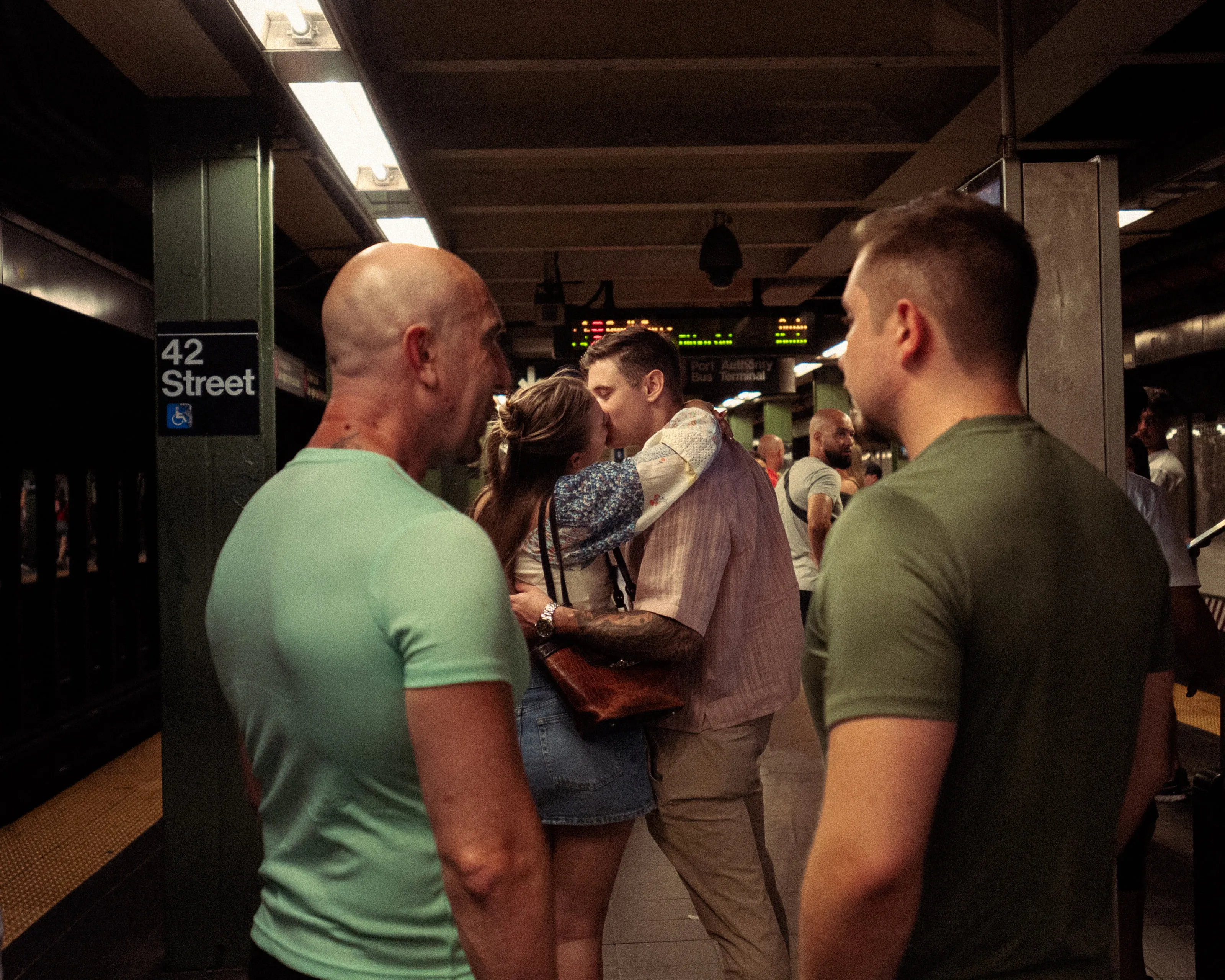 Three people talk closely on a late-night subway platform at 42nd Street.